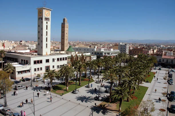 Vue de la place principale avec des palmiers, une tour horloge et des bâtiments traditionnels dans une ville ensoleillée
